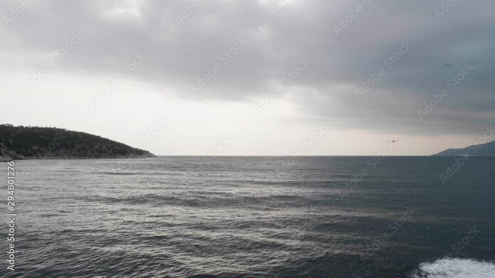 Flock of seagulls flying over cruise ship on open sea. Rocky island on open sea.
