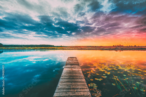 Landscape With Wooden Boards Pier On Calm Water Of Lake, River At Sunset Time, Forest On Other Side. Summer To Autumn Season Transition Concept In Nature