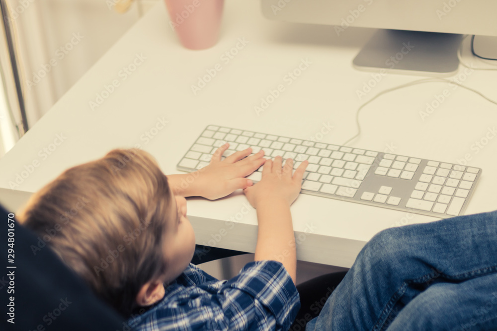 Small boy using computer and typing on a keyboard.