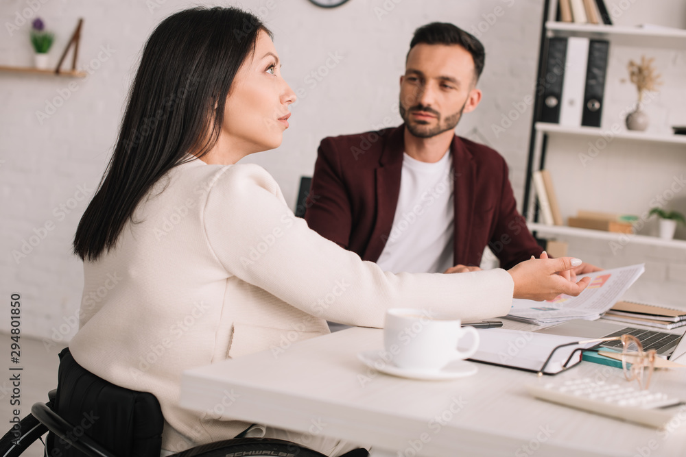 serious businesswoman looking up and gesturing while sitting at desk near handsome colleague serious businesswoman looking up and gesturing while sitting at desk near handsome colleague