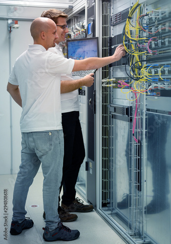 two IT professionals with notebook in server data center room solving a problem