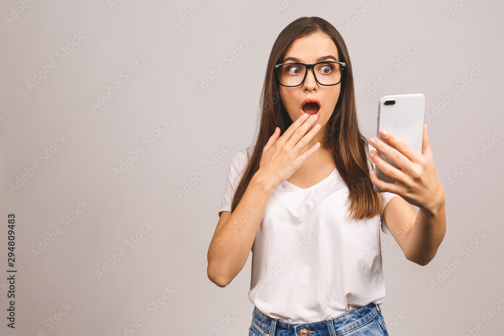 Portrait of a shocked amazed young girl using mobile phone isolated over grey background. Portrait of a shocked amazed young girl using mobile phone isolated over grey background.