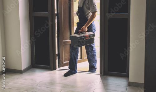 The repairer is coming in the house with toolbox in his hand