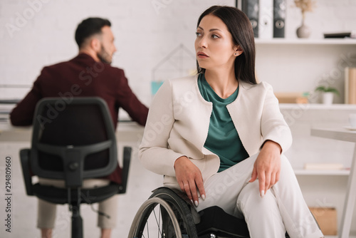 serious disabled businesswoman looking away while sitting in wheelchair in office near colleague © LIGHTFIELD STUDIOS