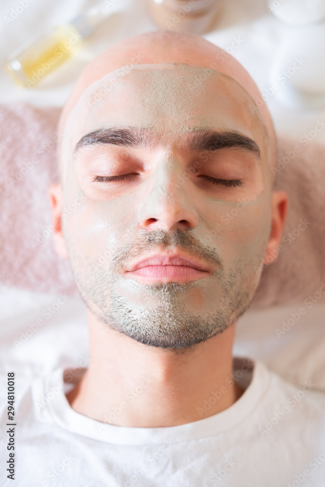 Obraz premium Man with green clay mask on his face. Male grooming, taking self care concept: applying natural treatment to skin