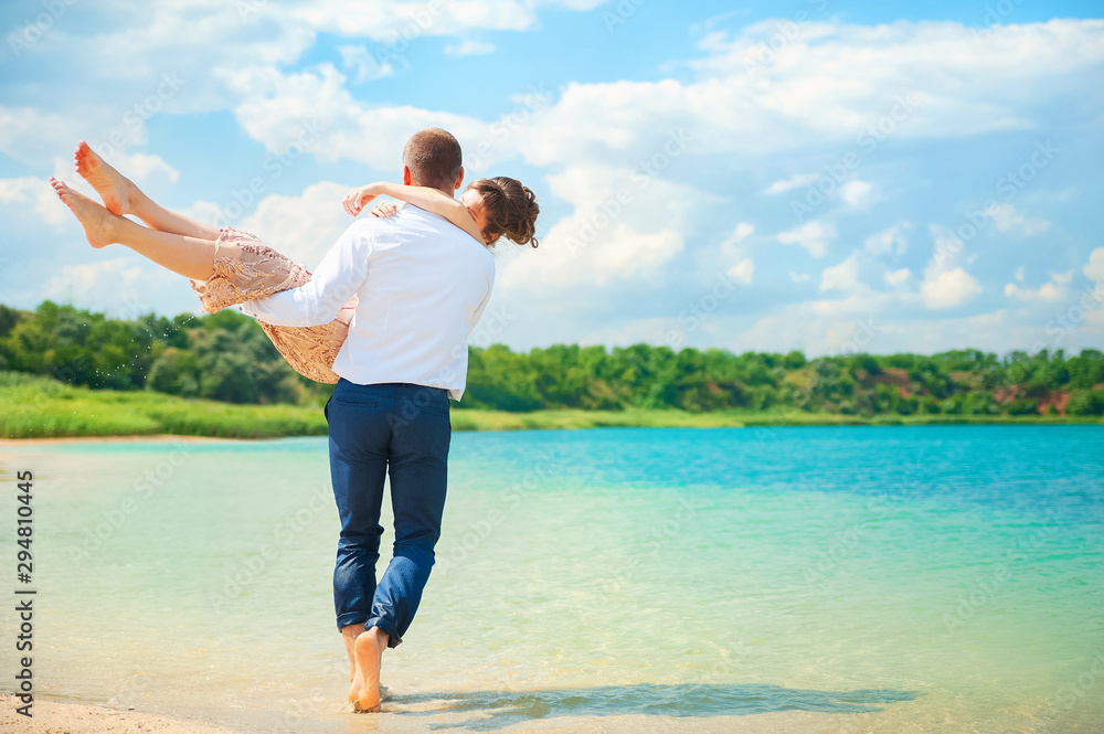 Idealistic poster for advertisement. Couple at the beach holding hands embracing and walking. Sunny day, bright colors. Photo from behind. Ukraine. Copy-spaced image of a cheerful young couple piggyba Idealistic poster for advertisement. Couple at the beach holding hands embracing and walking. Sunny day, bright colors. Photo from behind. Ukraine. Copy-spaced image of a cheerful young couple piggyba