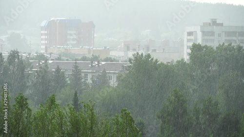 Summer heavy rain in city. Top view on green trees and roofs of houses. 4K video
