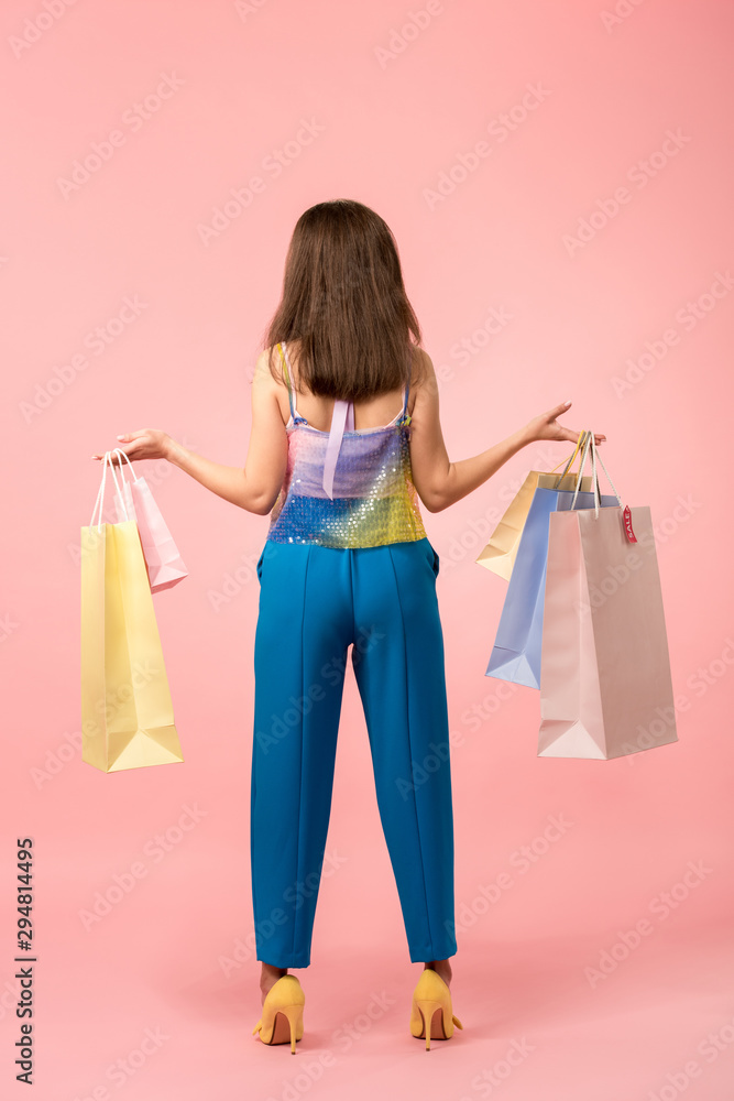 back view of happy stylish disco girl holding shopping bags on pink back view of happy stylish disco girl holding shopping bags on pink
