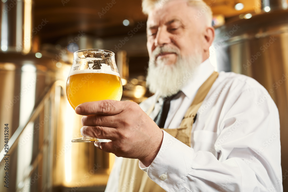 Elderly brewer holding glass with light beer.