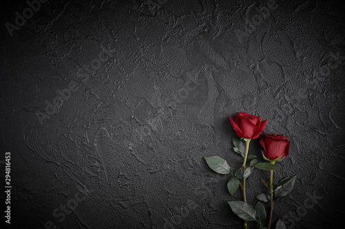 Red roses are placed on a black textured background. A sign of condolence, sympathy loss. Space for your text