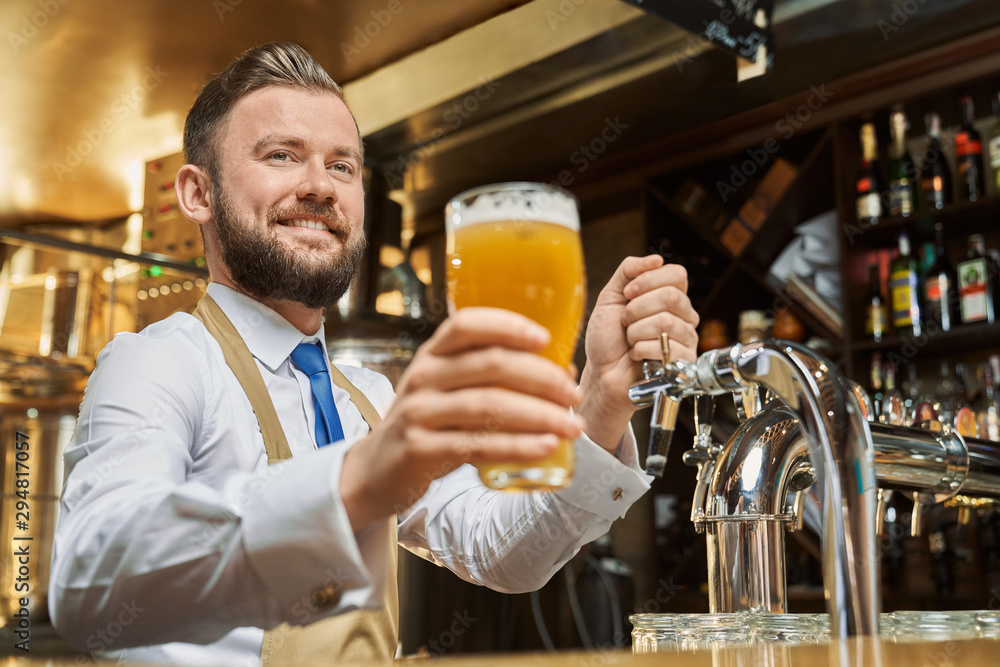 Handsome barman holding cold lager beer glass.