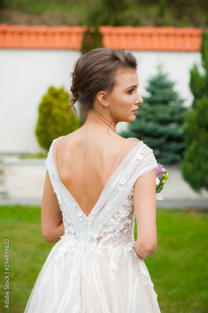 Naklejka premium Bride in long wedding dress with bouquet outdoor
