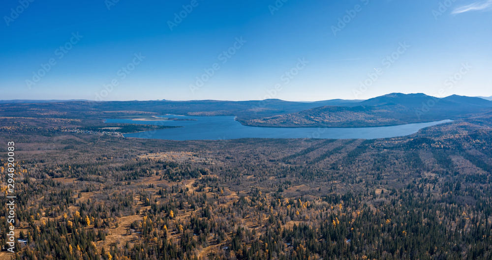 Aerial drone view of Zuratcul lake in autumn surrounded by Ural mountains, hills, mixed forest with green pines and yellow birchs; colorful trees on coasts; fragile ecosystem and anthropogenic impact