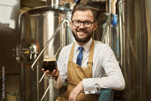 Fotografie Cheerful brewer posing with dark beer glass.