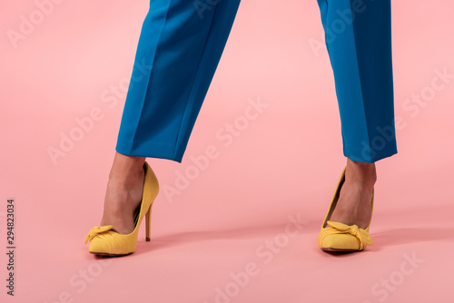 bottom view of young stylish disco girl in yellow heeled shoes and blue trousers on pink background