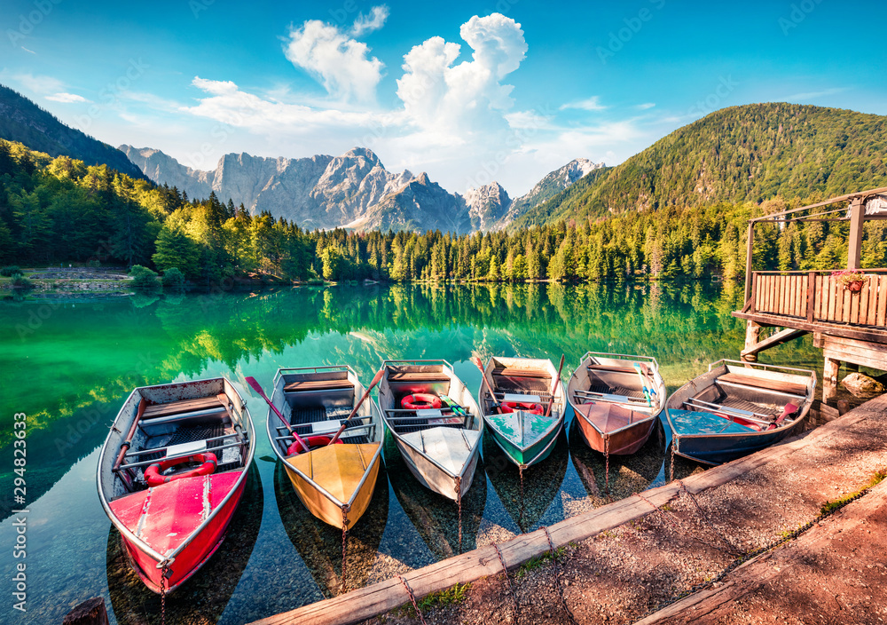Six pleasure boats on Fusine lake. Bright morning scene of Julian Alps with Mangart peak on background, Province of Udine, Italy, Europe. Traveling concept background.