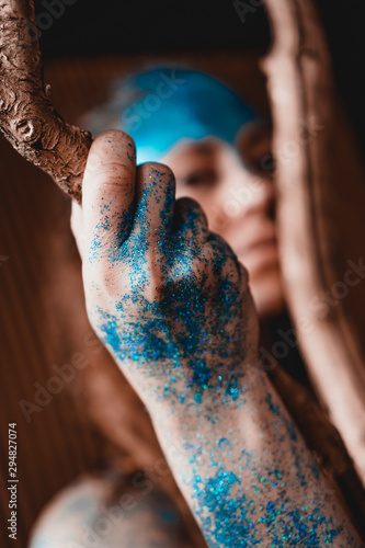 Portrait of a beautiful woman posing like in the wild forest. Woman with blue sparkles on her face. People are different from others. Individuality