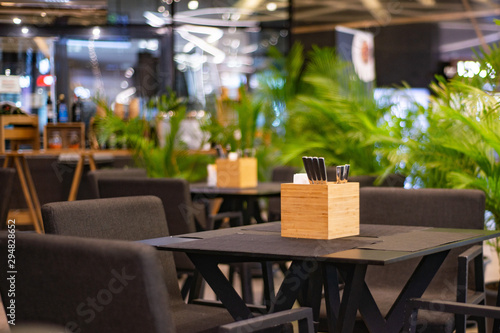 cafe with brown tables and chairs, tableware on the tables in the supplies, around the green indoor palm trees