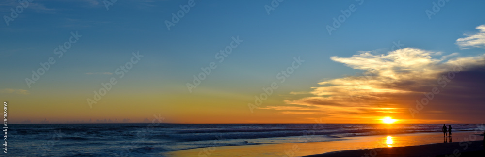 Wide panorama silhouette of people playing on the beach with beautiful sunset.