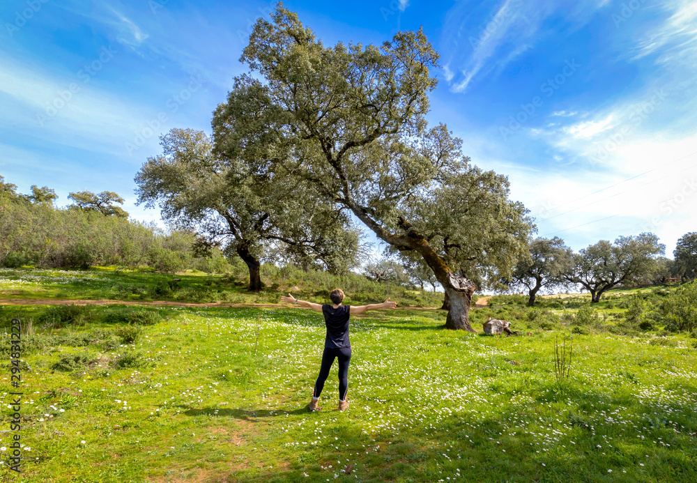 Young woman with her arms wide spread is enjoying in the sunny spring day, rear view. Freedom concept background.