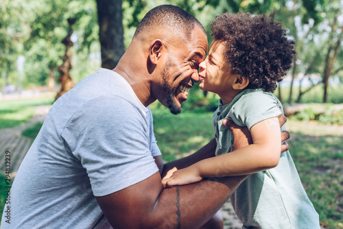 cute african american boy kissing happy father while having fun in park