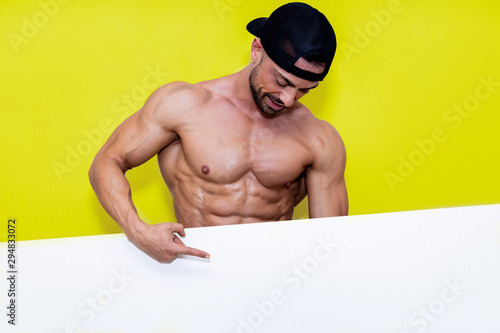 muscular man without shirt, pointing to a white poster he has in hand for copy space