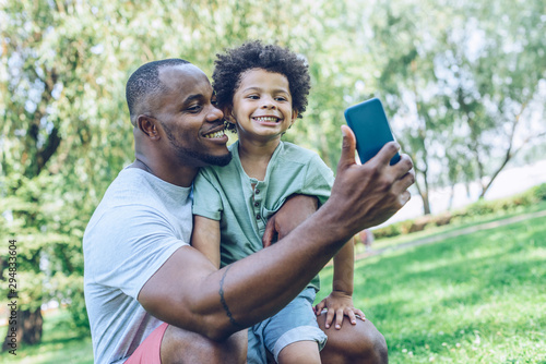 happy african american father and son taking selfie on smartphone in park © LIGHTFIELD STUDIOS