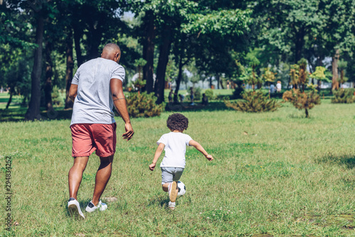 back view of african american father and son playing football in park