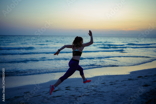 fit sports woman on ocean shore in evening jogging