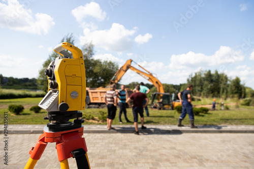 Side-view of yellow and orange tacheometer against working process on construction site photo