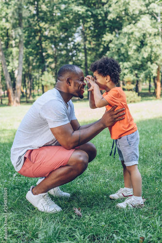 cheerful african american boy having fun with happy father in park