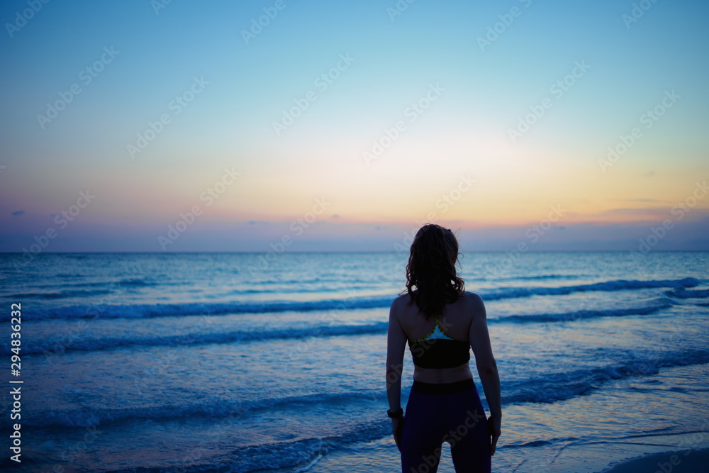 fit woman in sport clothes on seacoast in evening relaxing