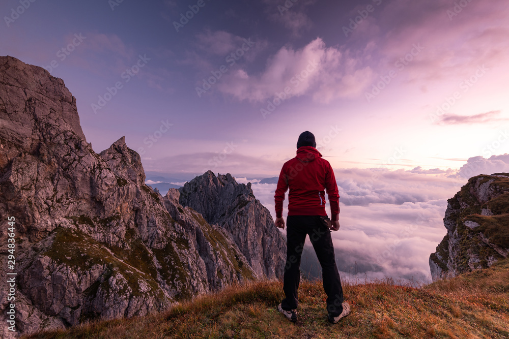 Adventure Hiker Looking at Clouds from Above from High Mountain Peak at Sunrise