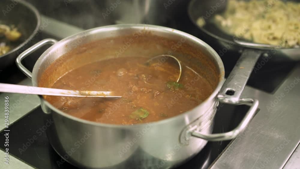 Close up handheld shot of chef male hand stirring a bowling soup in a pot in the kitchen stove in european restaurant. Stirring bowling soup close up Close up handheld shot of chef male hand stirring a bowling soup in a pot in the kitchen stove in european restaurant. Stirring bowling soup close up