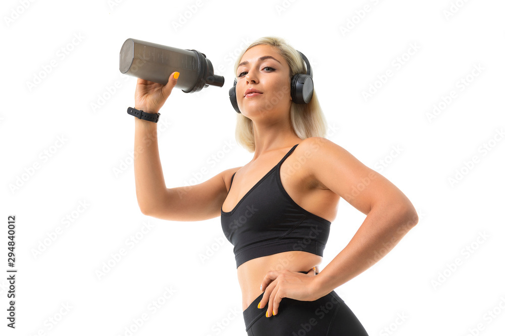 A sports girl with blonde hair and bright manicure in headphones, black sports topics and leggings holds a sports water bottle. A sports girl with blonde hair and bright manicure in headphones, black sports topics and leggings holds a sports water bottle.