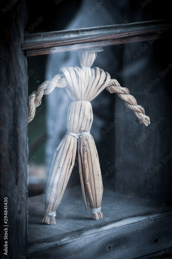 Straw man figurine hand made crafted behind the window on windowsill in an old house