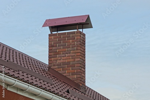 one large brown brown chimney pipe on a tiled roof against a blue sky