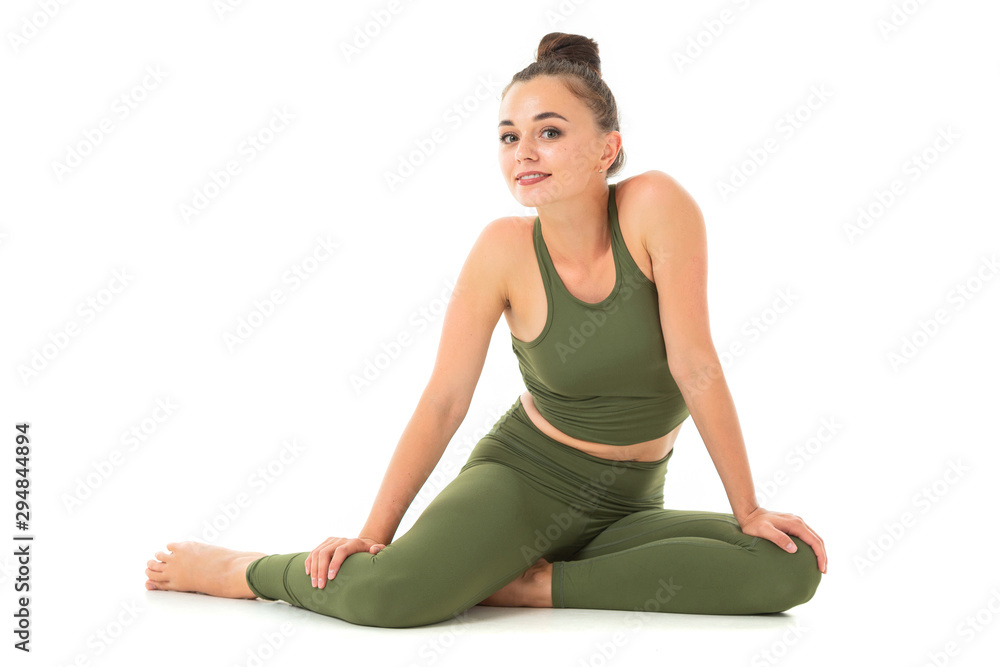 A beautiful young female gymnast with dark long hair stuffed into a bundle in a green sports elastic suit sits and smiling.