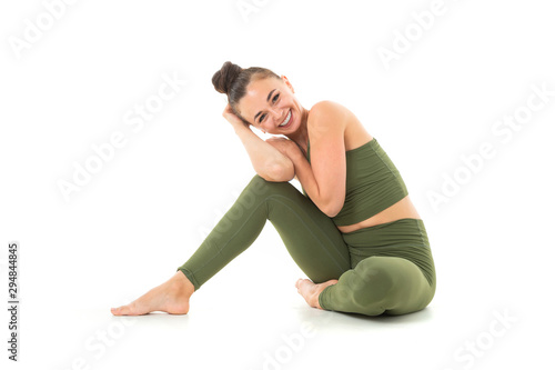 A beautiful young female gymnast with dark long hair stuffed into a bundle in a green sports elastic suit sits and smiling.
