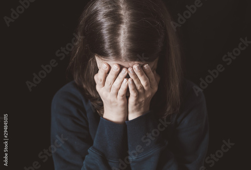 Wallpaper Mural Portrait of a crying woman covering her face with hands on a black background