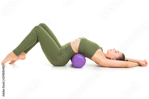 A beautiful young female gymnast with dark long hair stuffed into a bundle in a green sports elastic suit makes a stretch on various muscle groups with sporting inventory