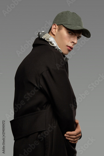 Medium close-up shot of a short-haired European man dressed in a dazzle hooded top, a black jacket and a moss green cotton baseball cap. photo