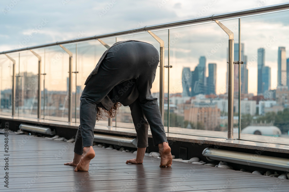 Attractive athletic man practicing yoga in business center with beautiful view on a city from skyscraper.