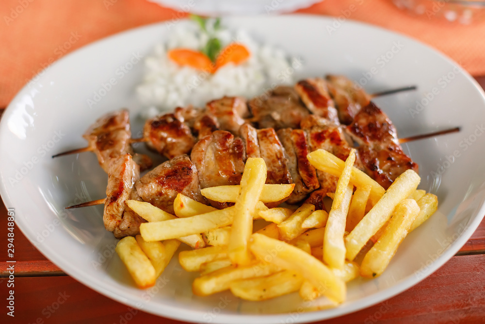 Plate with pork meat shish kebab and potatoes fries, closeup