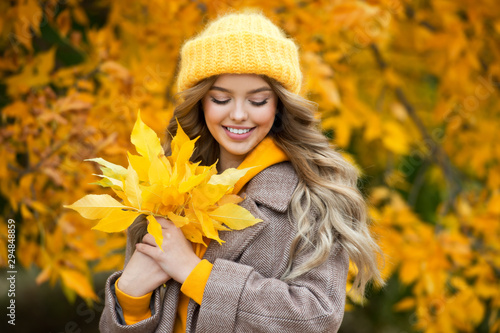 Beautiful girl walking outdoors in autumn. Smiling girl collects yellow leaves in autumn. Young woman enjoying autumn weather.