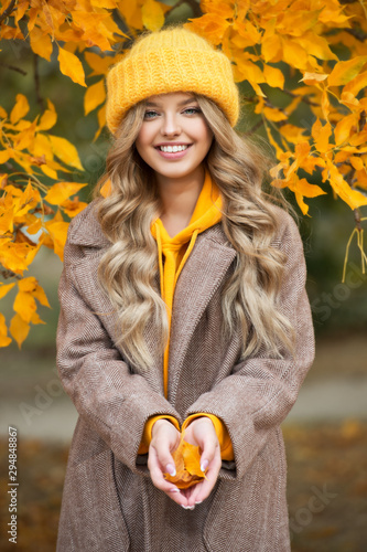 Beautiful girl walking outdoors in autumn. Smiling girl collects yellow leaves in autumn. Young woman enjoying autumn weather.