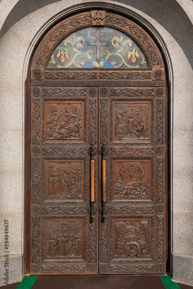 Wooden arched door of church with engraving of the scenes from Bible and stained glass