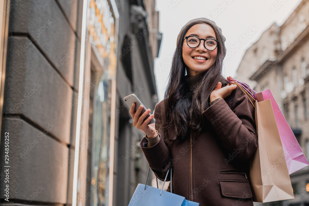 Asian woman using smartphone and looking away while enjoying a day shopping Asian woman using smartphone and looking away while enjoying a day shopping