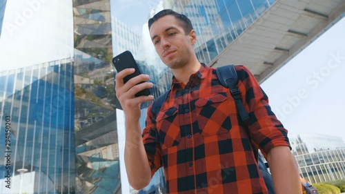 Close-up young man use phone in city. Tourist in red shirt using samrtphone on glass buinding background. photo