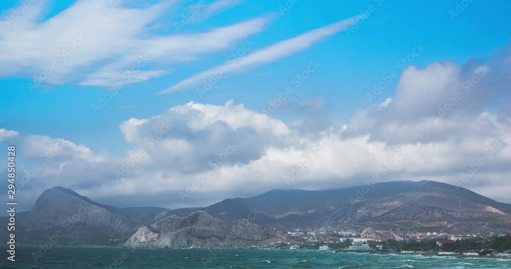 Cumulus clouds in motion in the Crimea over the mountains in the city of Sudak. Beach and sea on a summer day Cumulus clouds in motion in the Crimea over the mountains in the city of Sudak. Beach and sea on a summer day